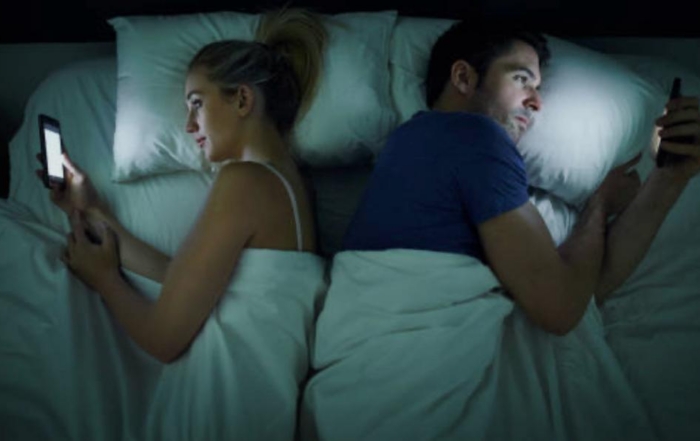 couple in bed facing away from one another on their phones
